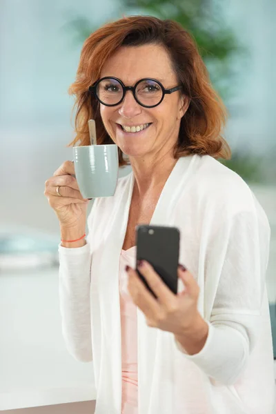 Зрелая Женщина Держит Кофе Использует Смартфон Доме — стоковое фото