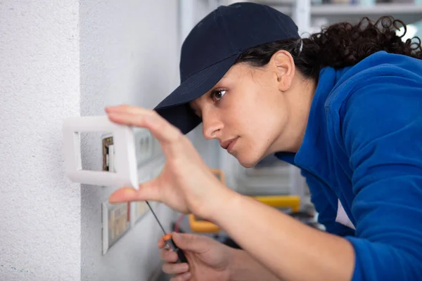 女性電気技師の笑顔が壁のソケットを設置し — ストック写真