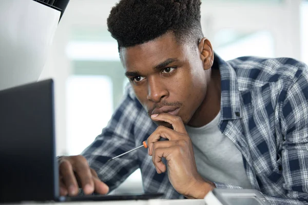 Homem Contemplativo Usando Laptop Segurando Uma Chave Fenda — Fotografia de Stock