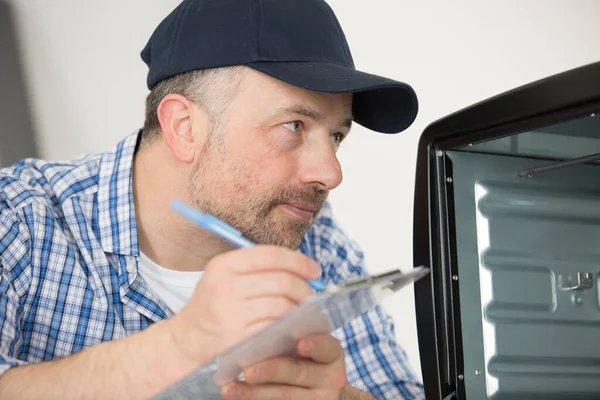 Mannelijke Elektricien Schrijven Klembord Tijdens Het Kijken Naar Oven — Stockfoto