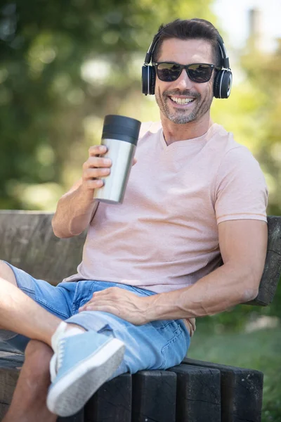 Mature Man Park Bench Holding Coffee Wearing Headphones — 스톡 사진