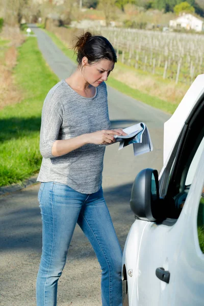 Kobieta Czytając Instrukcję Obsługi Pojazdu Przez Rozbity Samochód — Zdjęcie stockowe