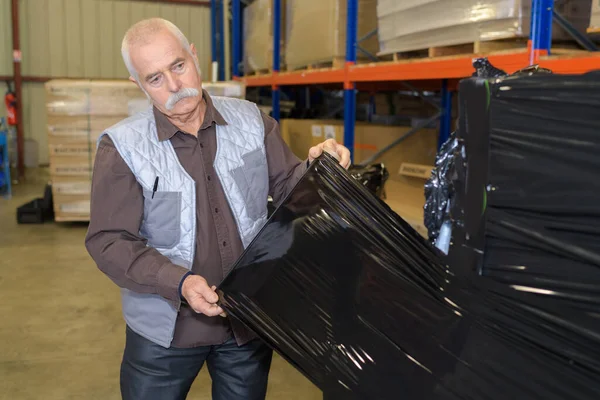 黒の収縮ラップに商品のパレットをカバーする上級倉庫労働者 — ストック写真