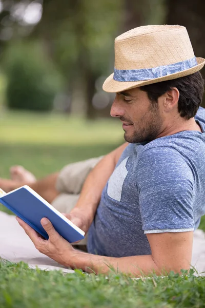 Man Reading Book Grass Wearing Hat — Zdjęcie stockowe