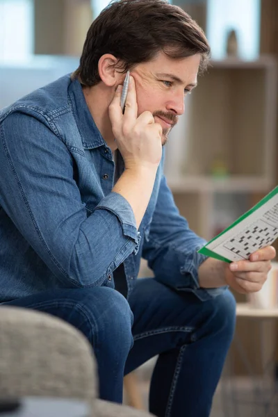 Man Sitting Doing Crossword Puzzle Looking Thoughtfully Magazine — Stock Photo, Image