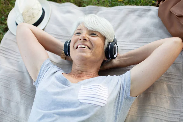 Mature Woman Listening Music While Laying Grass — стоковое фото