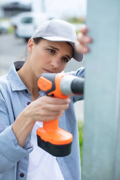 年轻的女建筑工人在墙上钻洞 — 图库照片