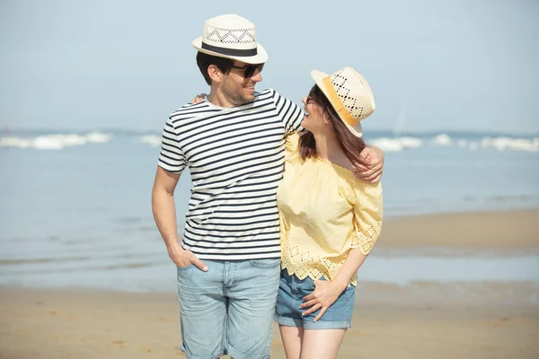 在海滩上散步的年轻夫妇互相牵着手笑着 — 图库照片