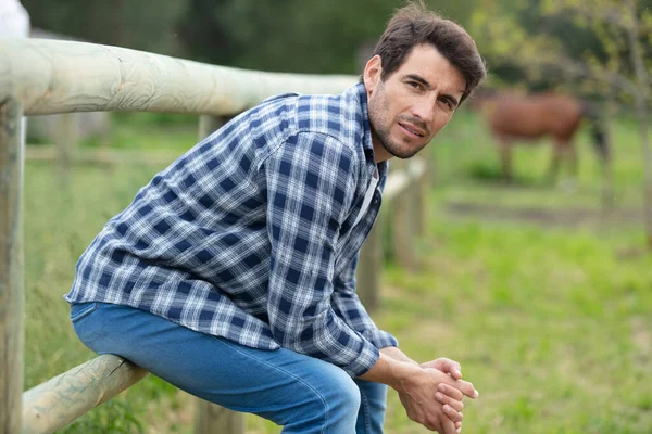 男子坐在农村农场的栅栏上 — 图库照片