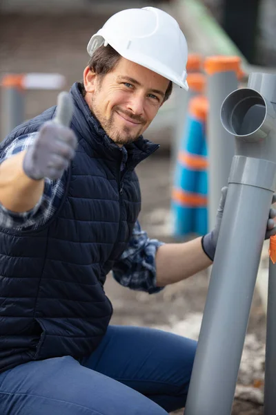 happy young plumber with waste pipes shows thumbs up