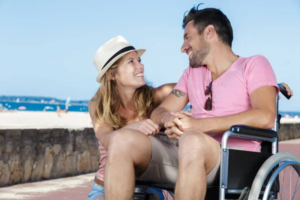 坐在轮椅上的海滨男子旁边的一对浪漫的年轻夫妇 — 图库照片