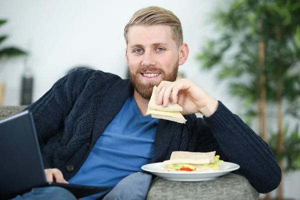 Hombre Usando Ordenador Portátil Mientras Come Sándwich Sofá —  Fotos de Stock