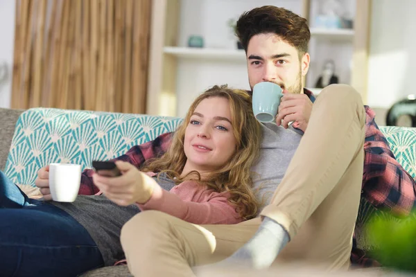 カップルはソファーでコーヒーを飲みテレビを見て — ストック写真