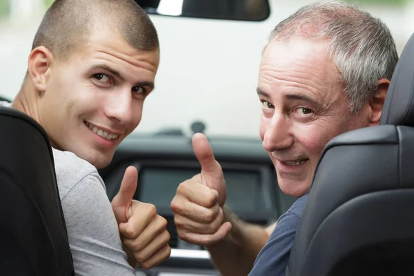 father and son in car looking back holding thumbs up