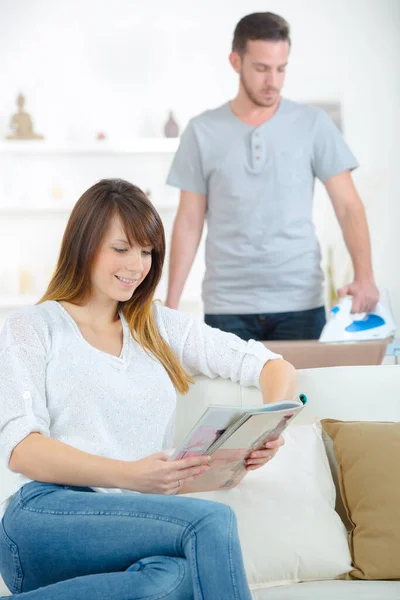 Man Doing Some Ironing While Girlfriend Reading — Stock Photo, Image