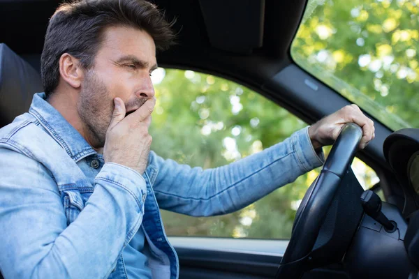 疲れた男が車の前の席であくびをしている — ストック写真