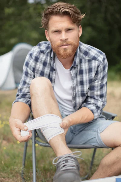 Wounded Man Bandaging Leg While Camping — Stock Photo, Image