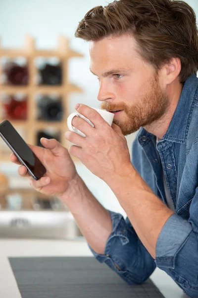 Muž Doma Pije Kávu Kontroluje Svůj Smartphone — Stock fotografie