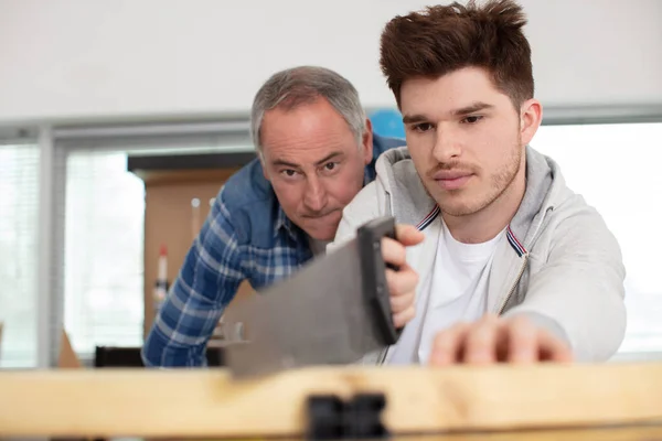 father carpenter teaches his son how to use a saw