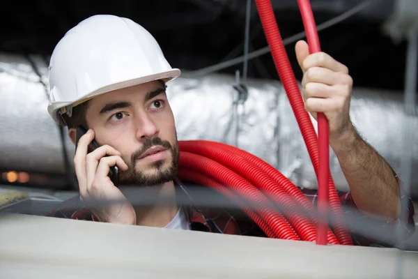 Builder Phone Working Ceiling Pipes — Stockfoto