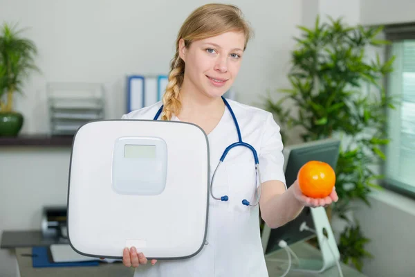 Female Doctor Holding Fruit Bathroom Scales — Stock Photo, Image