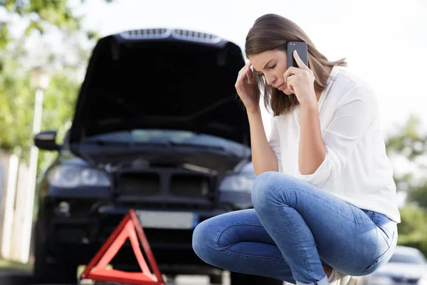 tensed woman using cell phone by broken down car