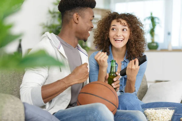 expressive couple with beer cheering for basketball game at home