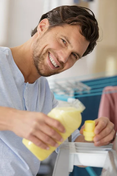 man pouring liquid laundry detergent in washing machine