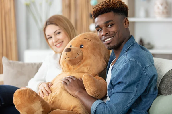 mixed couple sitting on sofa hugging teddy bear