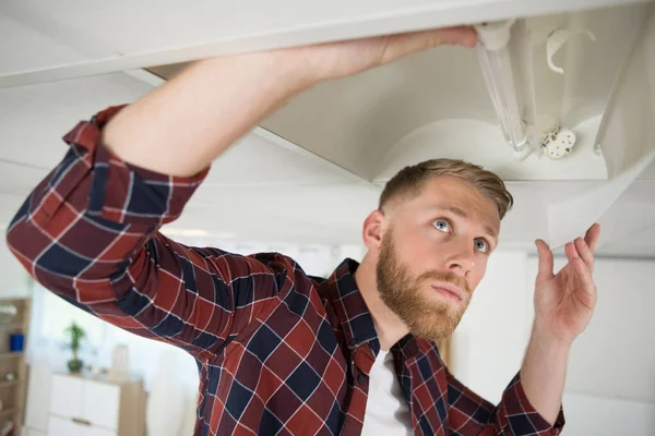 man change light bulb at ceiling lamp at home
