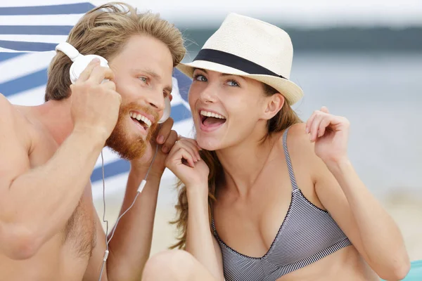 ヒップスターカップルはビーチでヘッドフォンで音楽を聴き — ストック写真