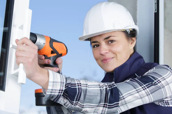 年轻的女建筑工人在新墙上钻洞 — 图库照片