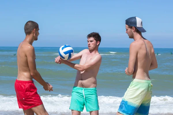 三个年轻人在海滩上打排球 — 图库照片