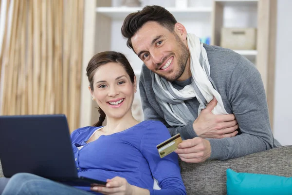 夫妻二人坐在沙发上看着笔记本电脑 手里拿着付款卡 — 图库照片
