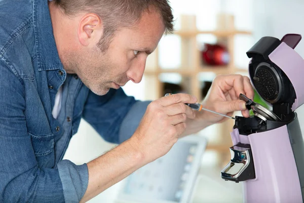 man repairing coffee machine by screwdriver in kitchen