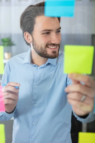 businessman through glass writing on post-it in office