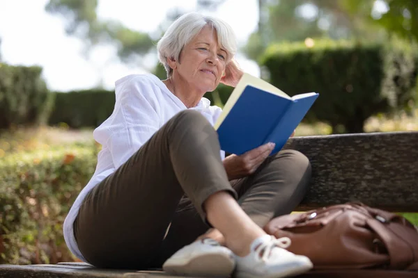 退休妇女在长椅上看书 — 图库照片
