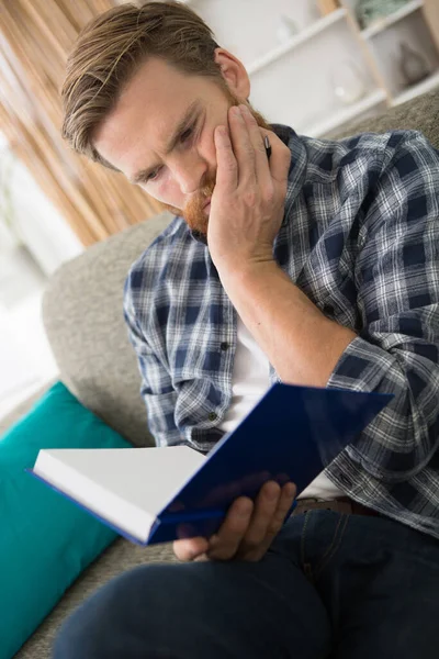 Avslappnad Ung Man Läser Bok Medan Sitter Vid Bokhyllan — Stockfoto