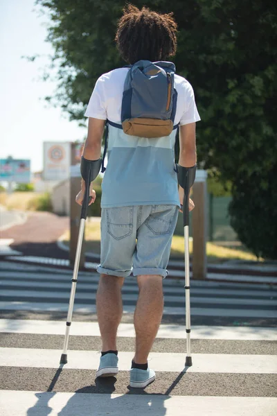 man with crutches crossing the road