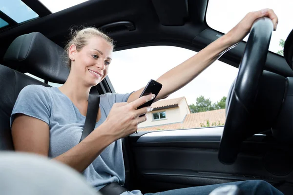年轻女人坐在车里看她的智能手机 — 图库照片