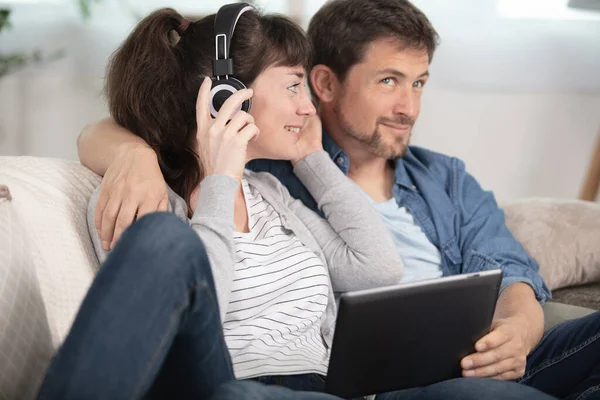 Sorrindo Casal Usando Laptop Usando Fones Ouvido Sentado Sofá — Fotografia de Stock