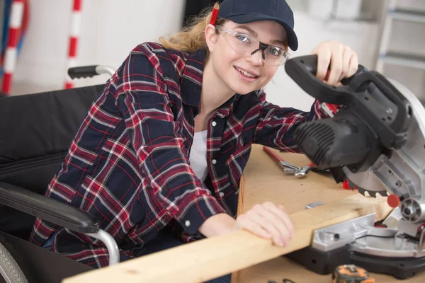 disable woman saws a wooden bar on a miter saw