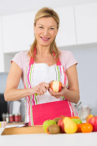 高齢者の女性が彼女のキッチンでリンゴを剥離 — ストック写真