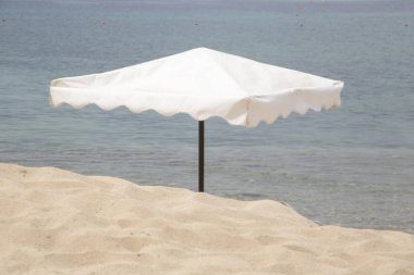 Kumlu sahilde beyaz retro tarzı şemsiye.