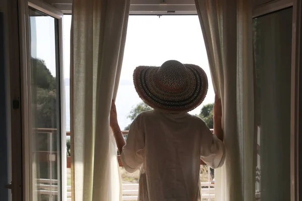 窓から外を眺めカーテンを開ける女性の背中 — ストック写真