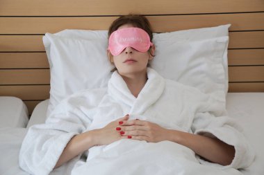 Pembe uyku maskesi takan ve yatakta dinlenen genç ve güzel bir kadın..