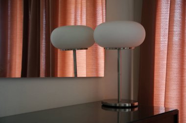 Masa lambası ve kadife perdeleri olan bir odanın şık ve karamsar görüntüsü.