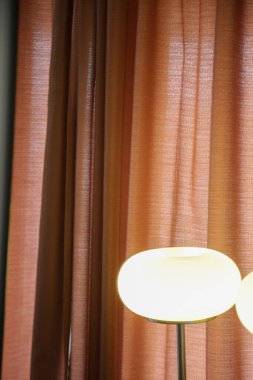 Masa lambası ve kadife perdeleri olan bir odanın şık ve karamsar görüntüsü.