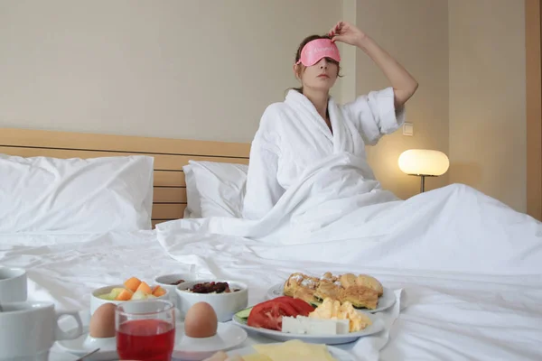 Pembe Uyku Maskeli Genç Bayan Yatakta Kahvaltı Yapıyor — Stok fotoğraf