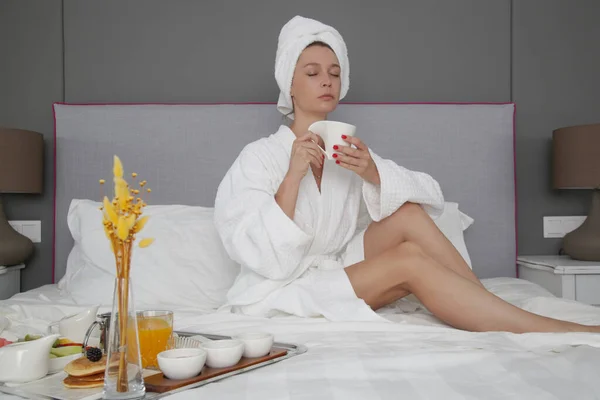 ベッドで朝のコーヒーを楽しむ若い女性 — ストック写真